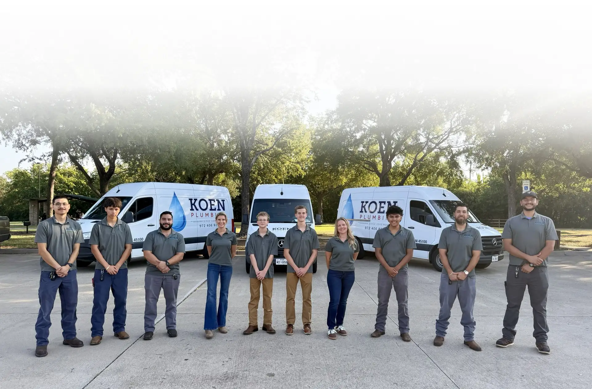 The Koen Plumbing team standing together in front of three Koen Plumbing service vans